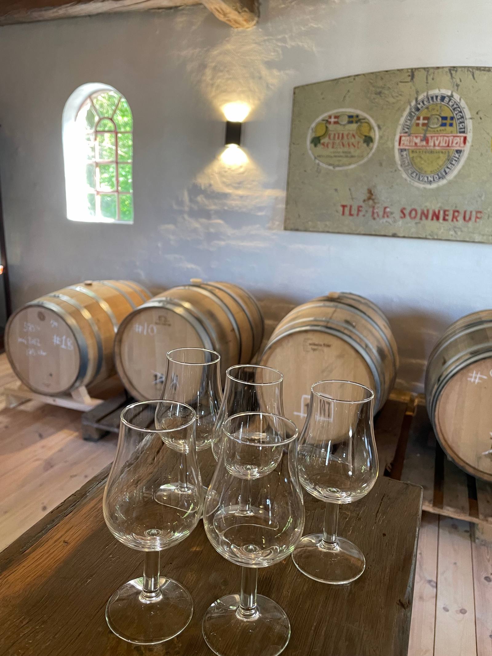 Det gamle emaljeskilt for Vintre Mølle Bryggeri & Mineralvandsfabrik på væggen i fadrummet, over fade og en række glas.